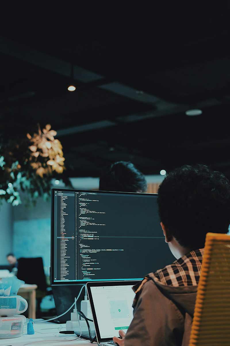 DevOps engineer working at a desk with multiple monitors, reviewing code and system logs in a modern, well-lit workspace
